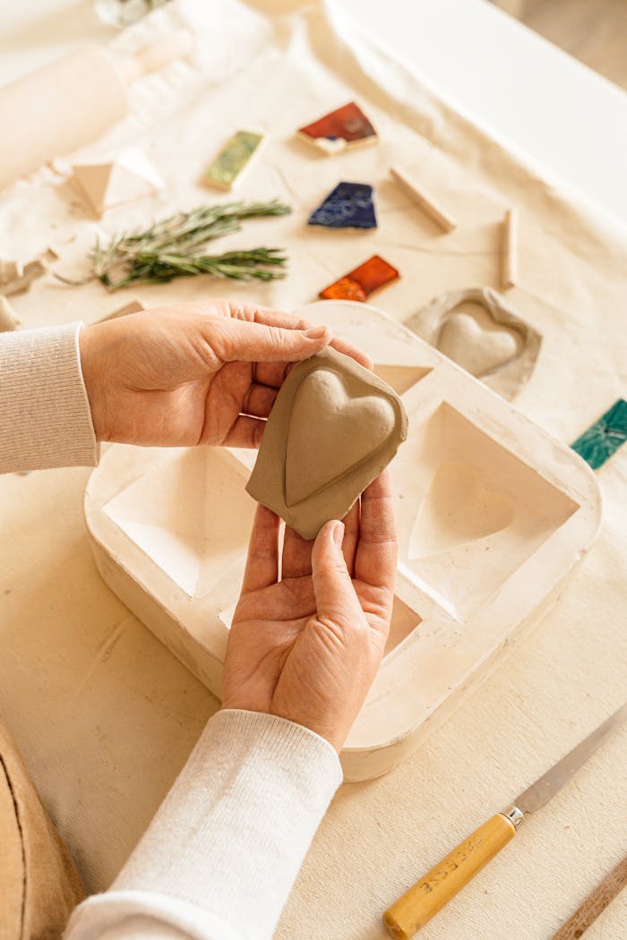 Close-up of hands shaping a ceramic heart soap mold with artisan decor.